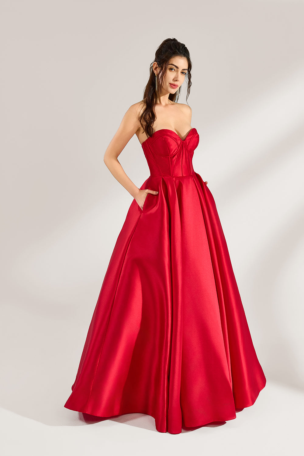 A woman stands against a light background, wearing a red satin strapless ball gown. The sweetheart neckline and voluminous skirt create an elegant and classic look, perfect for formal events like proms or weddings.4