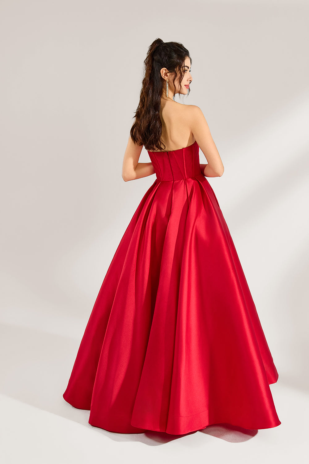 A woman stands against a light background, wearing a red satin strapless ball gown. The sweetheart neckline and voluminous skirt create an elegant and classic look, perfect for formal events like proms or weddings.2