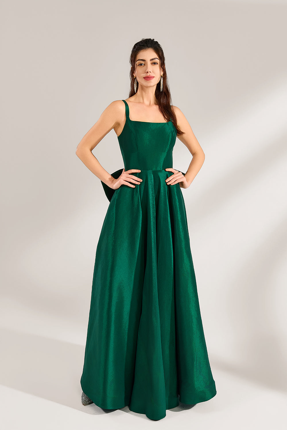 A woman stands against a light background, wearing a dark - green satin gown. It features square neckline, wide straps, and a bow at the waist. The voluminous skirt and elegant silhouette exude sophistication, perfect for formal events like galas or weddings, radiating timeless charm.3