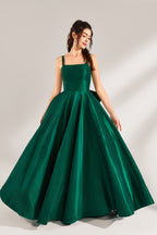 A woman stands against a light background, wearing a dark - green satin gown. It features square neckline, wide straps, and a bow at the waist. The voluminous skirt and elegant silhouette exude sophistication, perfect for formal events like galas or weddings, radiating timeless charm.1