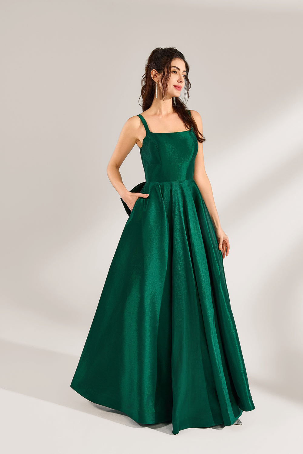 A woman stands against a light background, wearing a dark - green satin gown. It features square neckline, wide straps, and a bow at the waist. The voluminous skirt and elegant silhouette exude sophistication, perfect for formal events like galas or weddings, radiating timeless charm.4