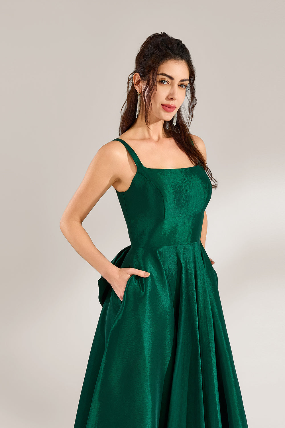 A woman stands against a light background, wearing a dark - green satin gown. It features square neckline, wide straps, and a bow at the waist. The voluminous skirt and elegant silhouette exude sophistication, perfect for formal events like galas or weddings, radiating timeless charm.5