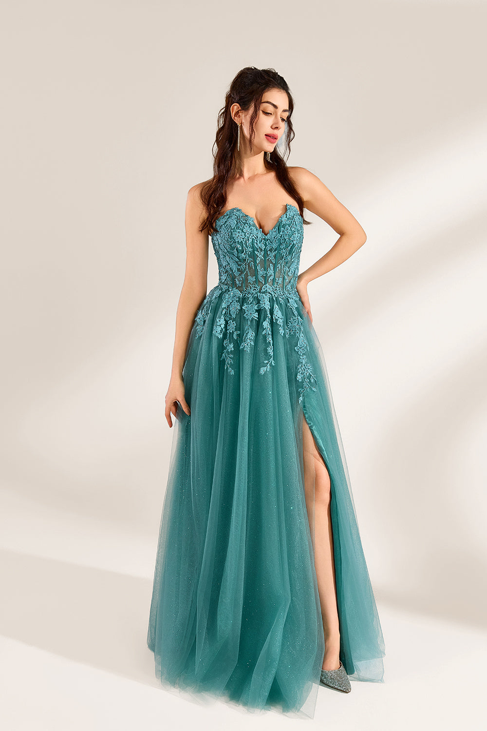 In front of a light - colored background, a woman is dressed in a teal tulle strapless gown. It has a sweetheart neckline, with the bodice adorned with delicate lace embroidery, and a high side slit. The voluminous tulle skirt, which has a slight shimmer, gives an elegant and romantic appearance, ideal for formal events such as proms or weddings.5