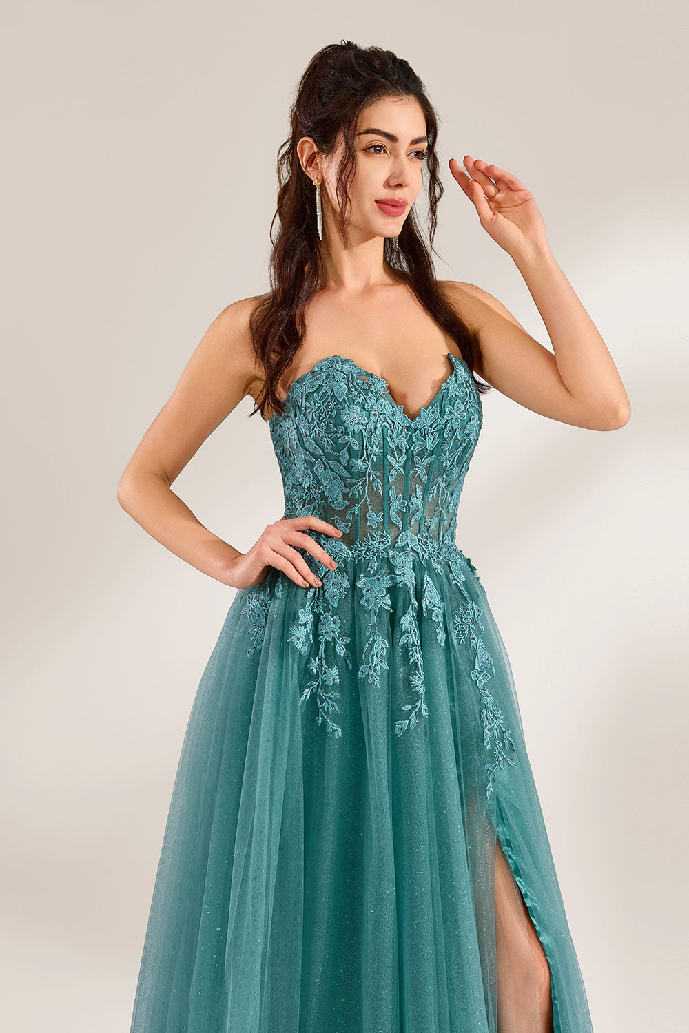 In front of a light - colored background, a woman is dressed in a teal tulle strapless gown. It has a sweetheart neckline, with the bodice adorned with delicate lace embroidery, and a high side slit. The voluminous tulle skirt, which has a slight shimmer, gives an elegant and romantic appearance, ideal for formal events such as proms or weddings.7