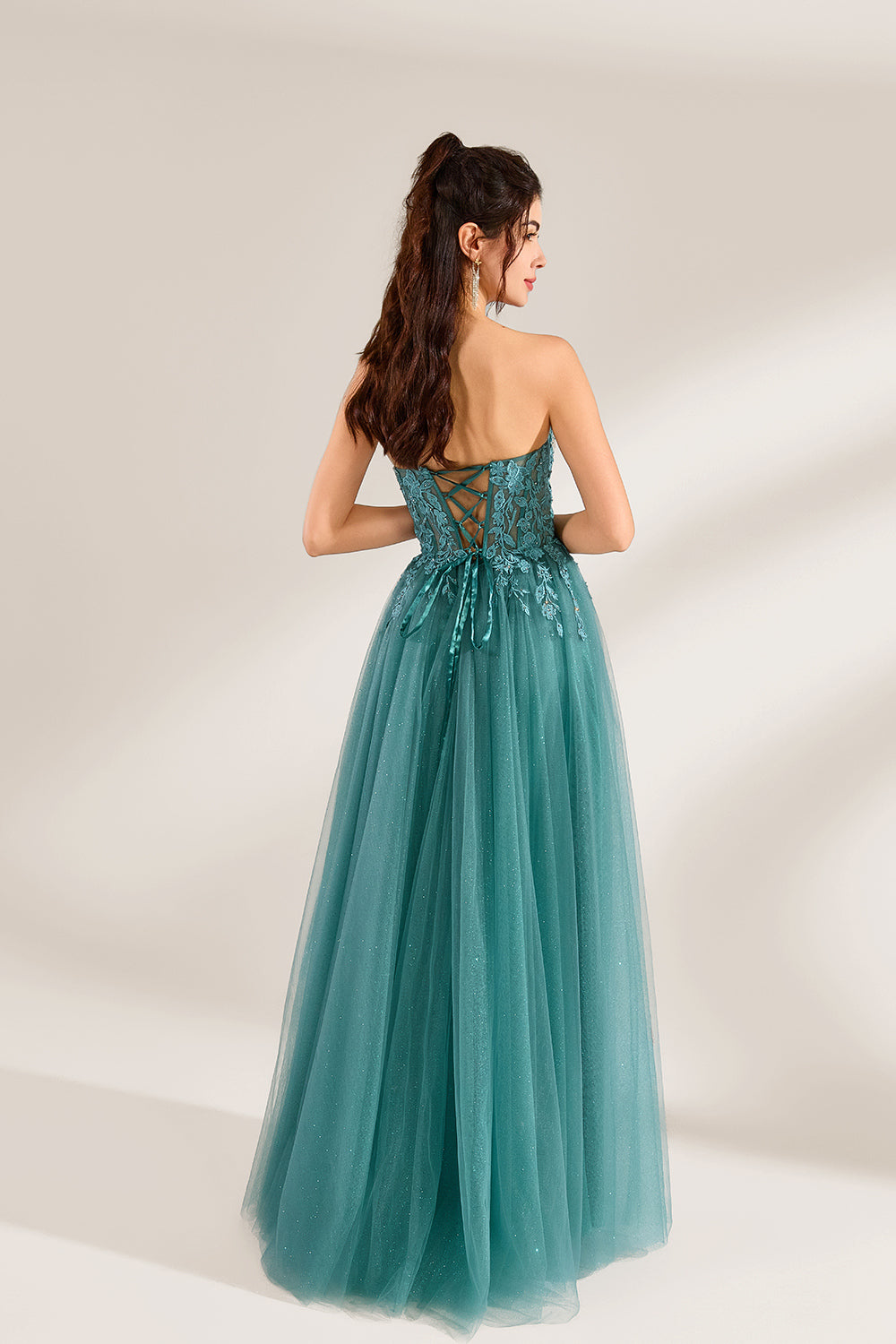 In front of a light - colored background, a woman is dressed in a teal tulle strapless gown. It has a sweetheart neckline, with the bodice adorned with delicate lace embroidery, and a high side slit. The voluminous tulle skirt, which has a slight shimmer, gives an elegant and romantic appearance, ideal for formal events such as proms or weddings.2