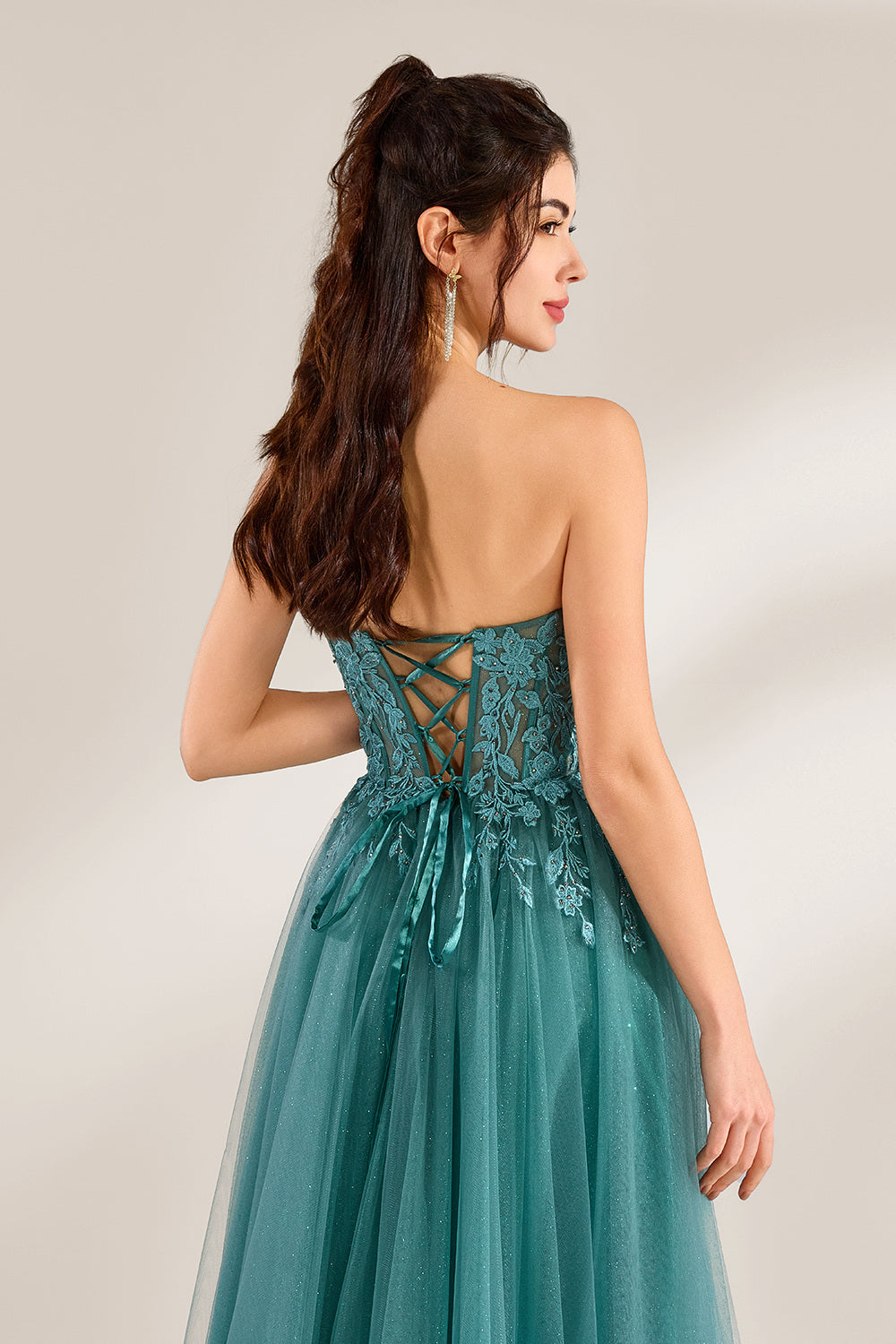 In front of a light - colored background, a woman is dressed in a teal tulle strapless gown. It has a sweetheart neckline, with the bodice adorned with delicate lace embroidery, and a high side slit. The voluminous tulle skirt, which has a slight shimmer, gives an elegant and romantic appearance, ideal for formal events such as proms or weddings.4