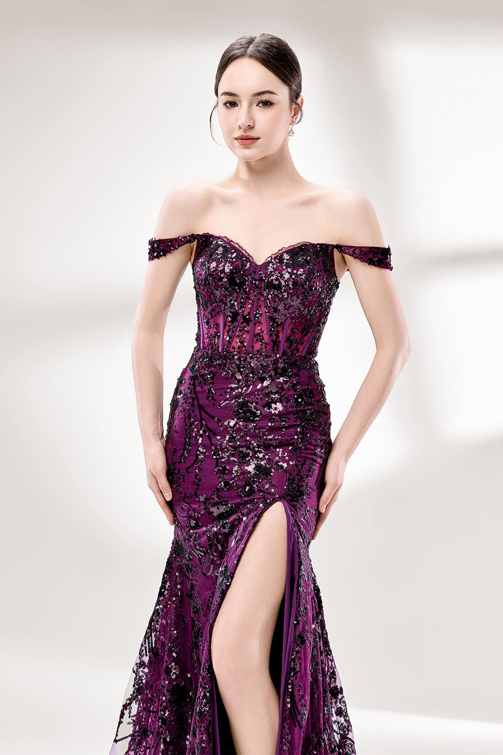 Set against a light background, a woman wears a purple tulle gown embellished with sequin embroidery. It has thin straps, a sweetheart neckline, a sheer bodice patterned with florals, and a mermaid skirt with a high side slit. Silver heels complete the look, with the sparkling sequins and refined silhouette ideal for proms or formal dinners.6