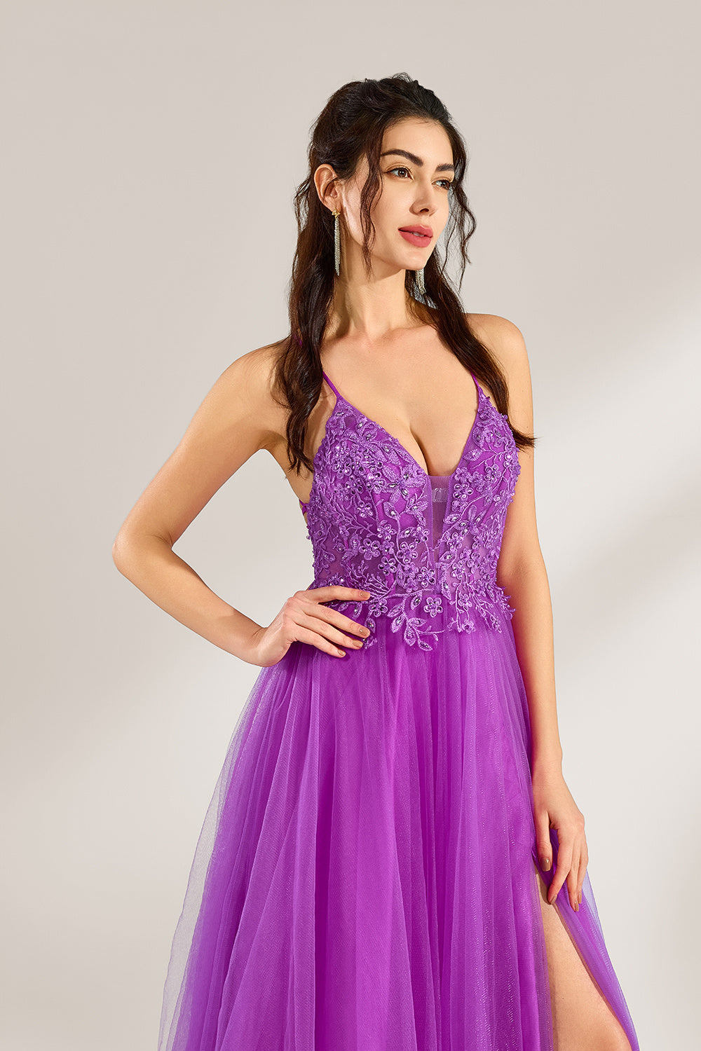Set against a light background, a woman adorns a purple tulle gown. It has thin straps, a deep V - neckline with delicate lace embroidery on the bodice, and a high side slit. The flowing tulle skirt gives off an elegant and romantic vibe, ideal for formal events such as proms or weddings.4