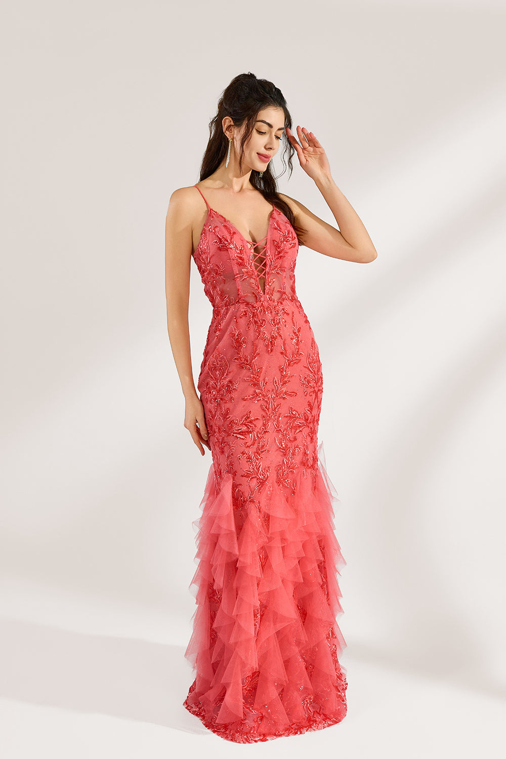 A woman stands against a light background, wearing a coral - pink tulle and lace mermaid gown. It features thin straps, a deep V - neckline with lace - up details, and intricate floral embroidery. The layered, ruffled tulle skirt creates a romantic and glamorous look, perfect for formal events like proms or weddings.3