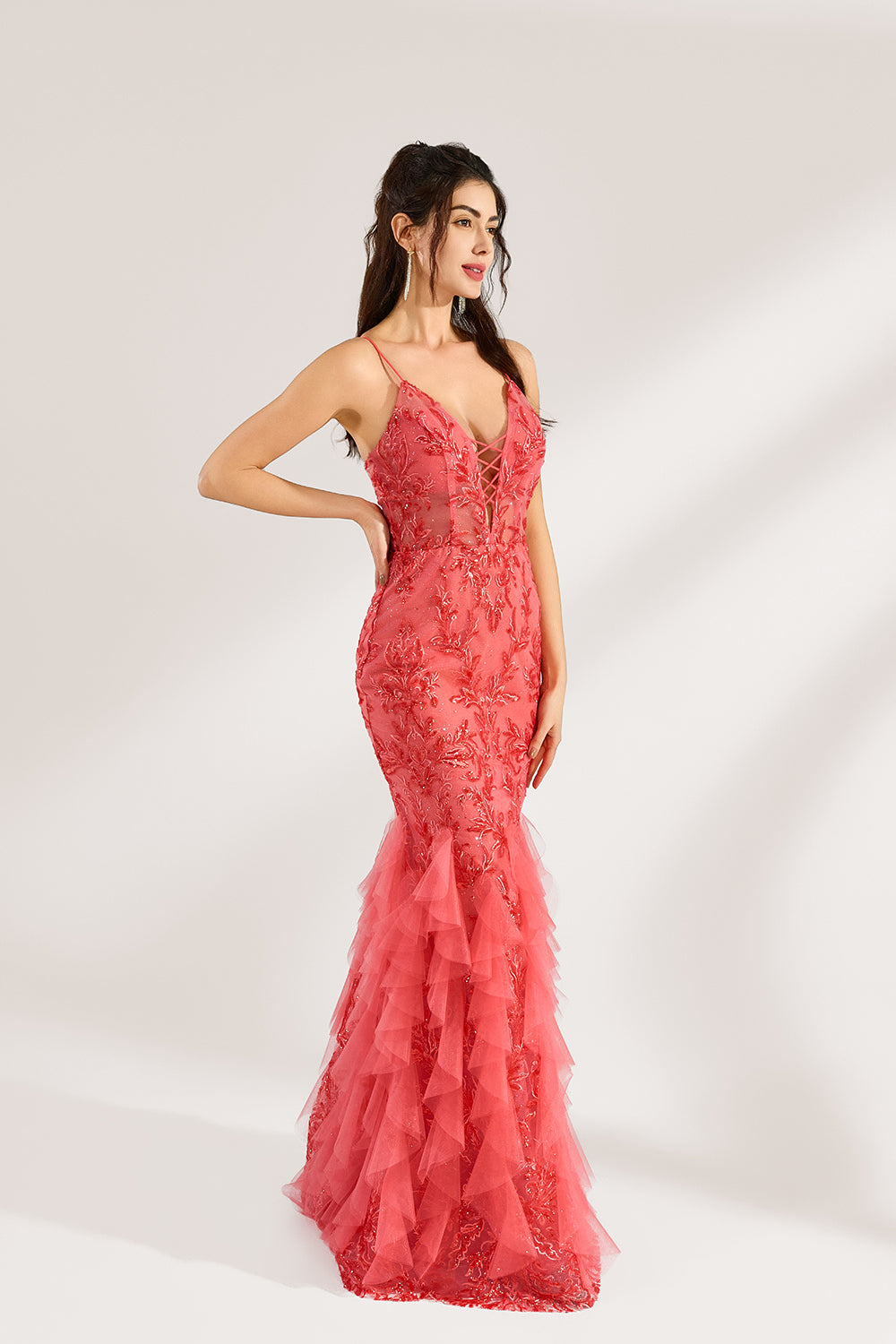 A woman stands against a light background, wearing a coral - pink tulle and lace mermaid gown. It features thin straps, a deep V - neckline with lace - up details, and intricate floral embroidery. The layered, ruffled tulle skirt creates a romantic and glamorous look, perfect for formal events like proms or weddings.1