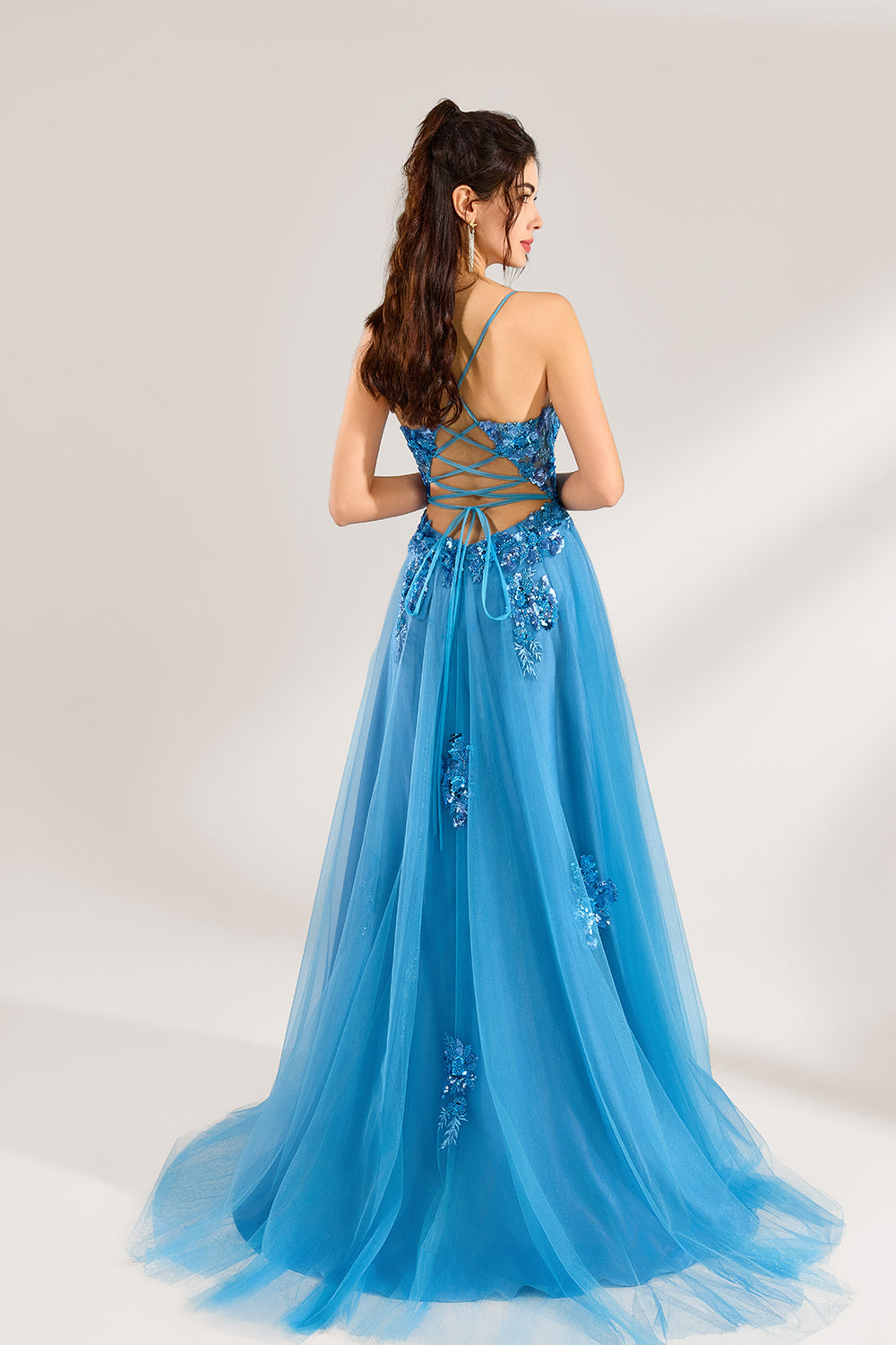 A woman stands against a light background, wearing a blue tulle gown. It features thin straps, a deep V - neckline, intricate floral appliqués with sequins on the bodice, and a high side slit. The voluminous tulle skirt creates a romantic and glamorous look, perfect for formal events like proms or weddings.2