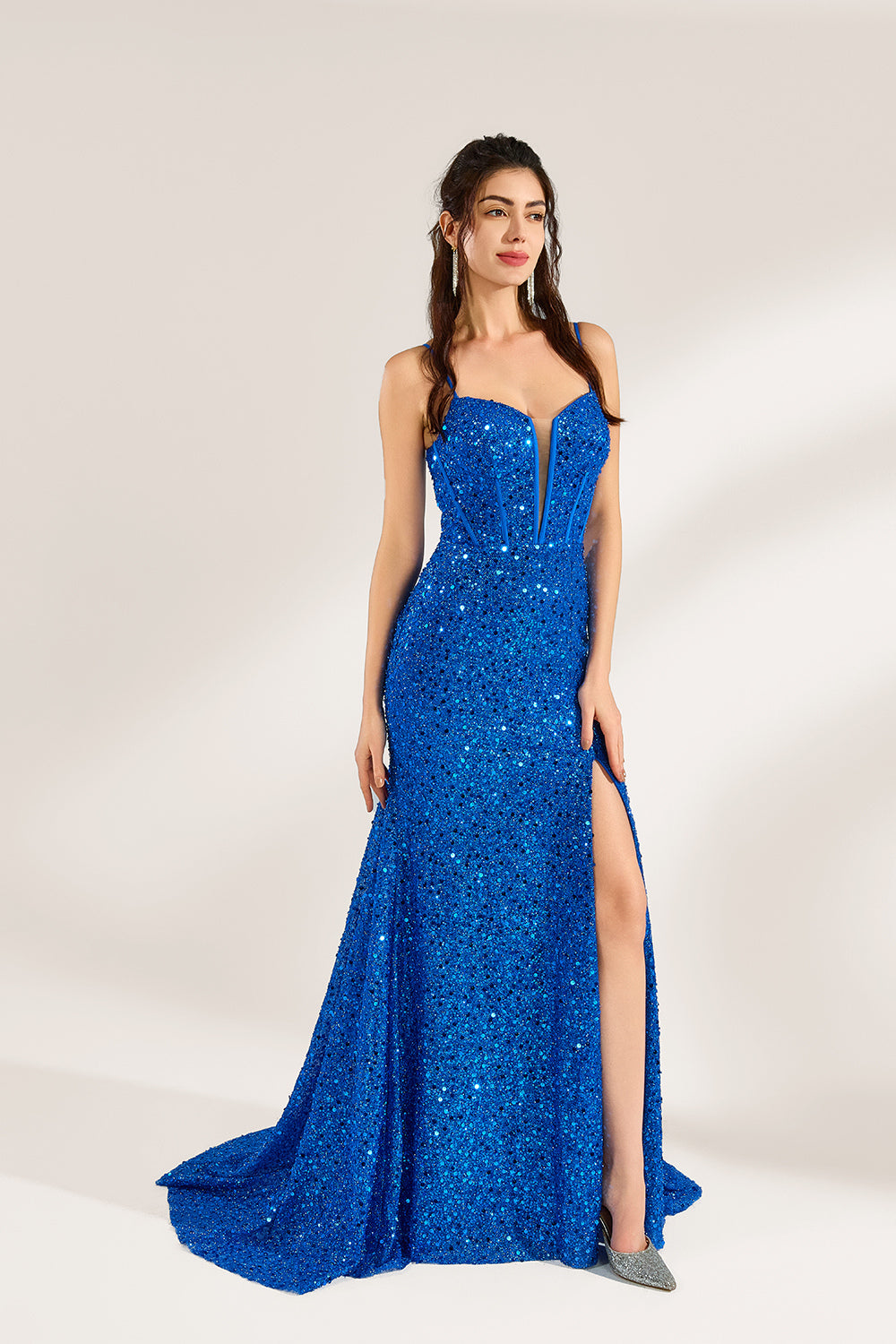 A woman stands against a light background, wearing a royal - blue sequin - covered mermaid gown. It features thin straps, a deep V - neckline with sheer panels, and a high side slit. The sparkling sequins create a glamorous look, perfect for formal events like galas or proms, exuding elegance and charm.1