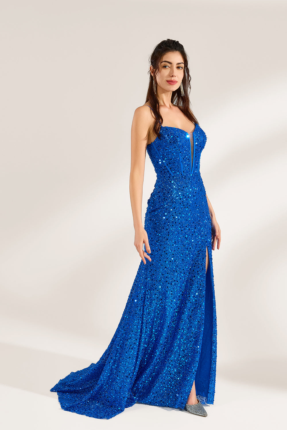 A woman stands against a light background, wearing a royal - blue sequin - covered mermaid gown. It features thin straps, a deep V - neckline with sheer panels, and a high side slit. The sparkling sequins create a glamorous look, perfect for formal events like galas or proms, exuding elegance and charm.5