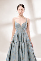 A woman stands against a light background, wearing a light - blue, tiered gown with gold - toned feather patterns. It has thin straps, a deep V - neckline, and a voluminous skirt. The unique jacquard design and elegant silhouette exude romance, perfect for formal events like garden parties or daytime weddings.5