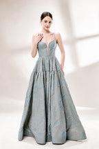 A woman stands against a light background, wearing a light - blue, tiered gown with gold - toned feather patterns. It has thin straps, a deep V - neckline, and a voluminous skirt. The unique jacquard design and elegant silhouette exude romance, perfect for formal events like garden parties or daytime weddings.4