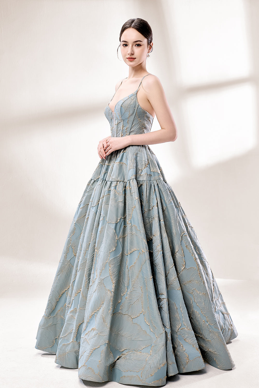 A woman stands against a light background, wearing a light - blue, tiered gown with gold - toned feather patterns. It has thin straps, a deep V - neckline, and a voluminous skirt. The unique jacquard design and elegant silhouette exude romance, perfect for formal events like garden parties or daytime weddings.3