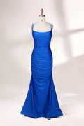 Photograph of a blue, floor-length evening gown displayed on a white dress form. The gown is sleeveless with a fitted bodice and a flared skirt, featuring thin shoulder straps and a textured, ruched design. The dress form is placed against a plain, off-white background, casting soft shadows.01