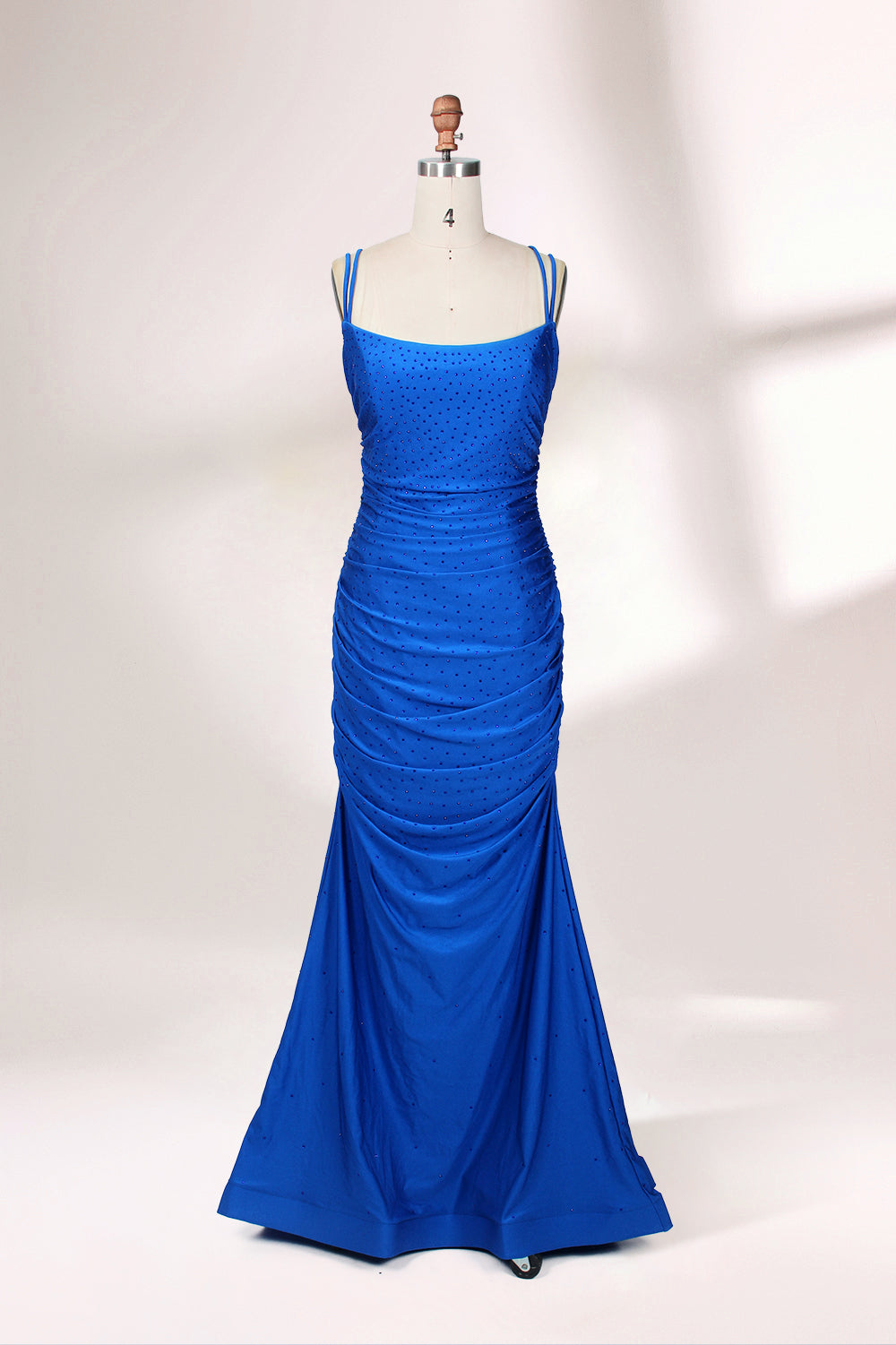 Photograph of a blue, floor-length evening gown displayed on a white dress form. The gown is sleeveless with a fitted bodice and a flared skirt, featuring thin shoulder straps and a textured, ruched design. The dress form is placed against a plain, off-white background, casting soft shadows.01