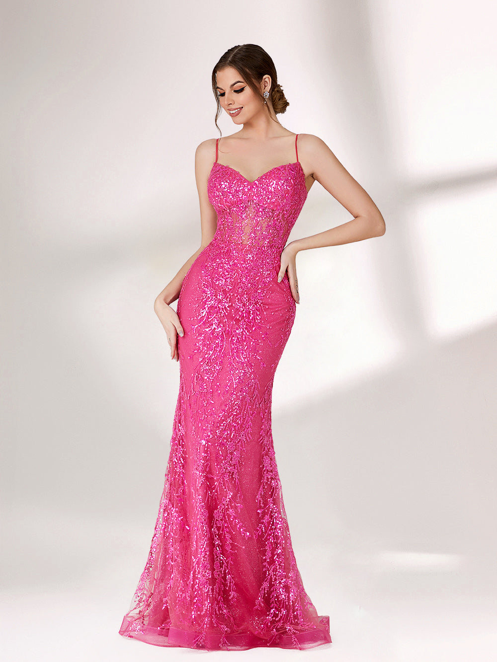 A woman stands against a light background, wearing a bright pink mermaid - style evening gown. It features thin spaghetti straps, a sweetheart neckline, and is covered in shimmering sequins with a sheer, embellished bodice detail. The elegant and glamorous design is perfect for formal events.1