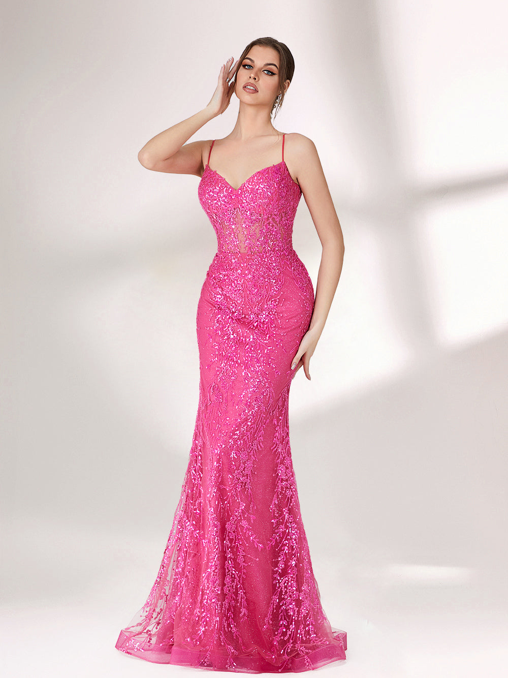 A woman stands against a light background, wearing a bright pink mermaid - style evening gown. It features thin spaghetti straps, a sweetheart neckline, and is covered in shimmering sequins with a sheer, embellished bodice detail. The elegant and glamorous design is perfect for formal events.3