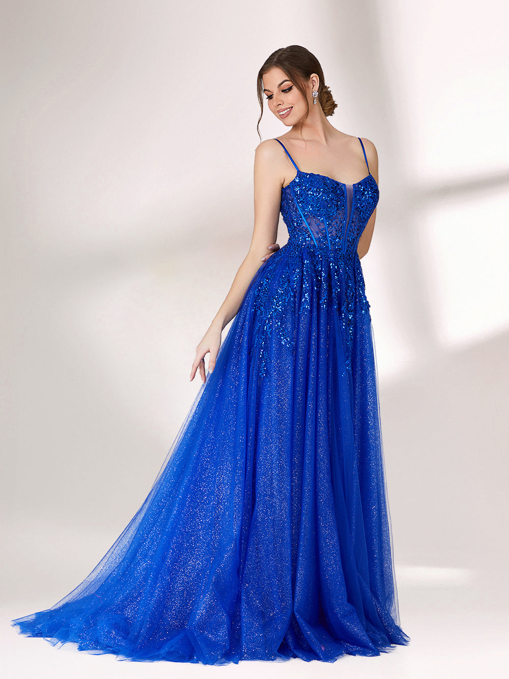 A woman stands against a light background, wearing a bright blue evening gown. It features thin spaghetti straps, a sweetheart neckline with a sheer, sequin - embellished bodice, and a voluminous tulle skirt that shimmers. The elegant design is perfect for formal events.5
