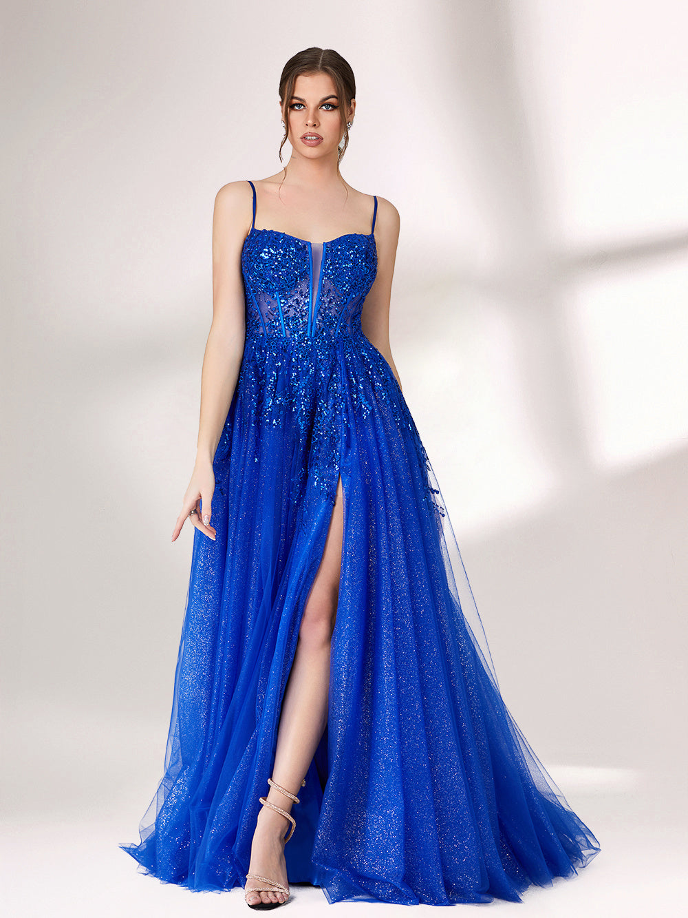 A woman stands against a light background, wearing a bright blue evening gown. It features thin spaghetti straps, a sweetheart neckline with a sheer, sequin - embellished bodice, and a voluminous tulle skirt that shimmers. The elegant design is perfect for formal events.6