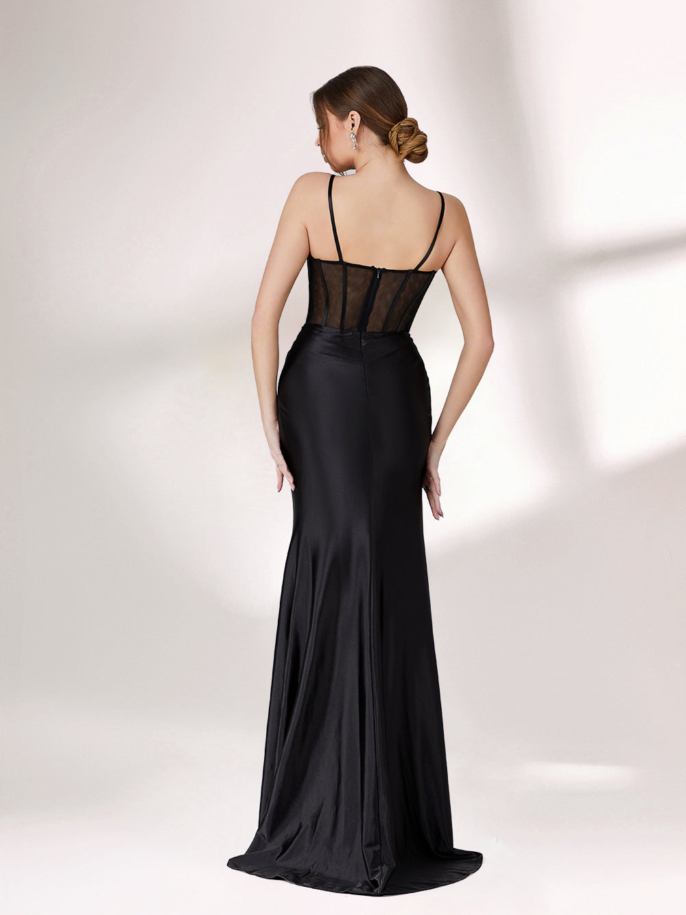A woman poses against a light background, wearing a black evening gown. It has thin spaghetti straps, a corset - style bodice with sheer mesh detailing, and a high - slit satin skirt. The design is sexy and elegant, perfect for formal events.4