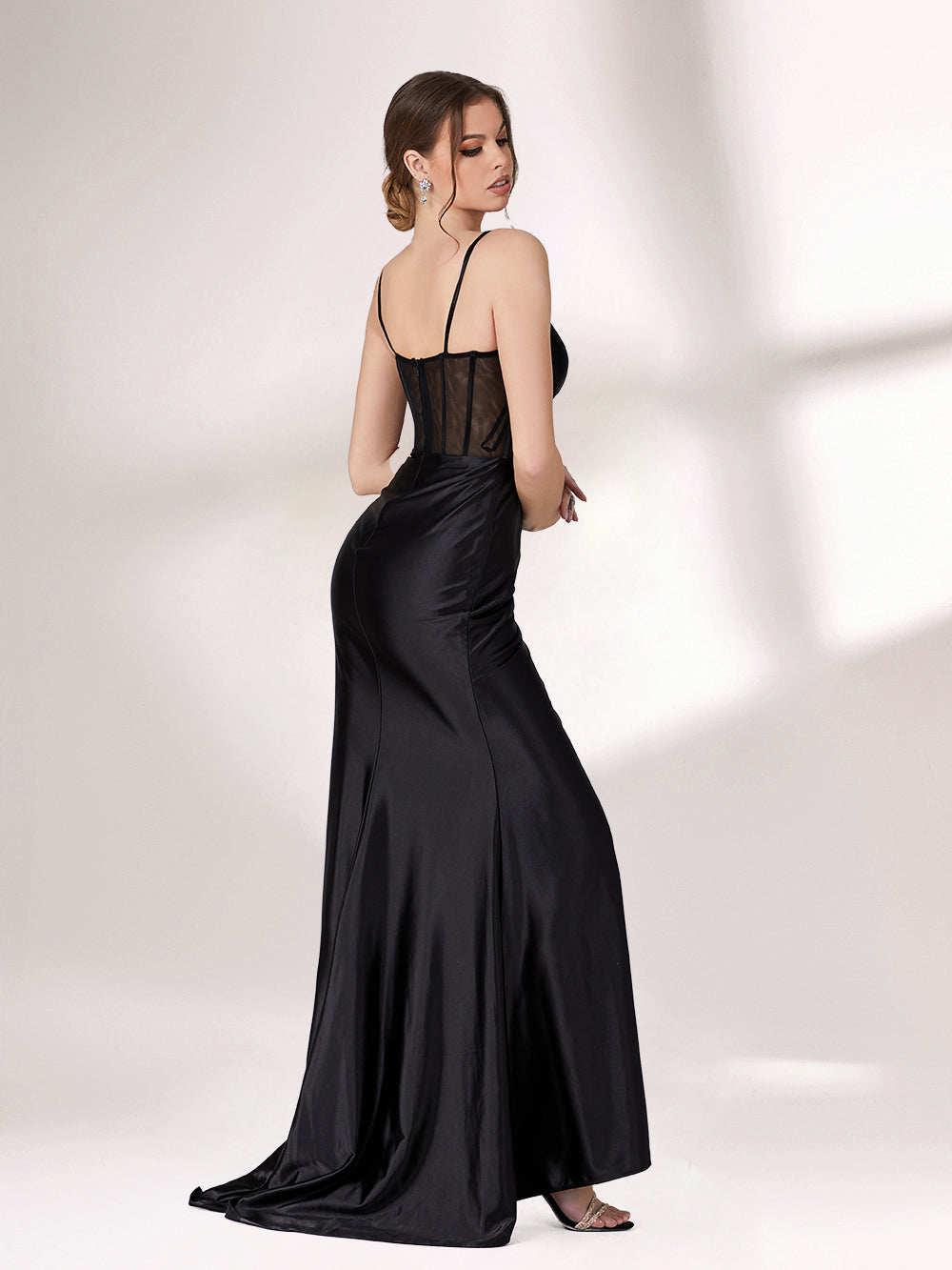 A woman poses against a light background, wearing a black evening gown. It has thin spaghetti straps, a corset - style bodice with sheer mesh detailing, and a high - slit satin skirt. The design is sexy and elegant, perfect for formal events.2