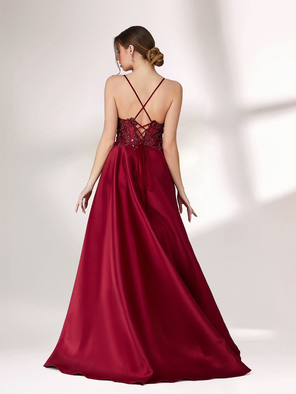 Bathed in soft light, a woman radiates elegance in a burgundy evening gown. With satin fabric, spaghetti straps, and lace embroidery, it crafts a luxurious and refined look for formal events.1