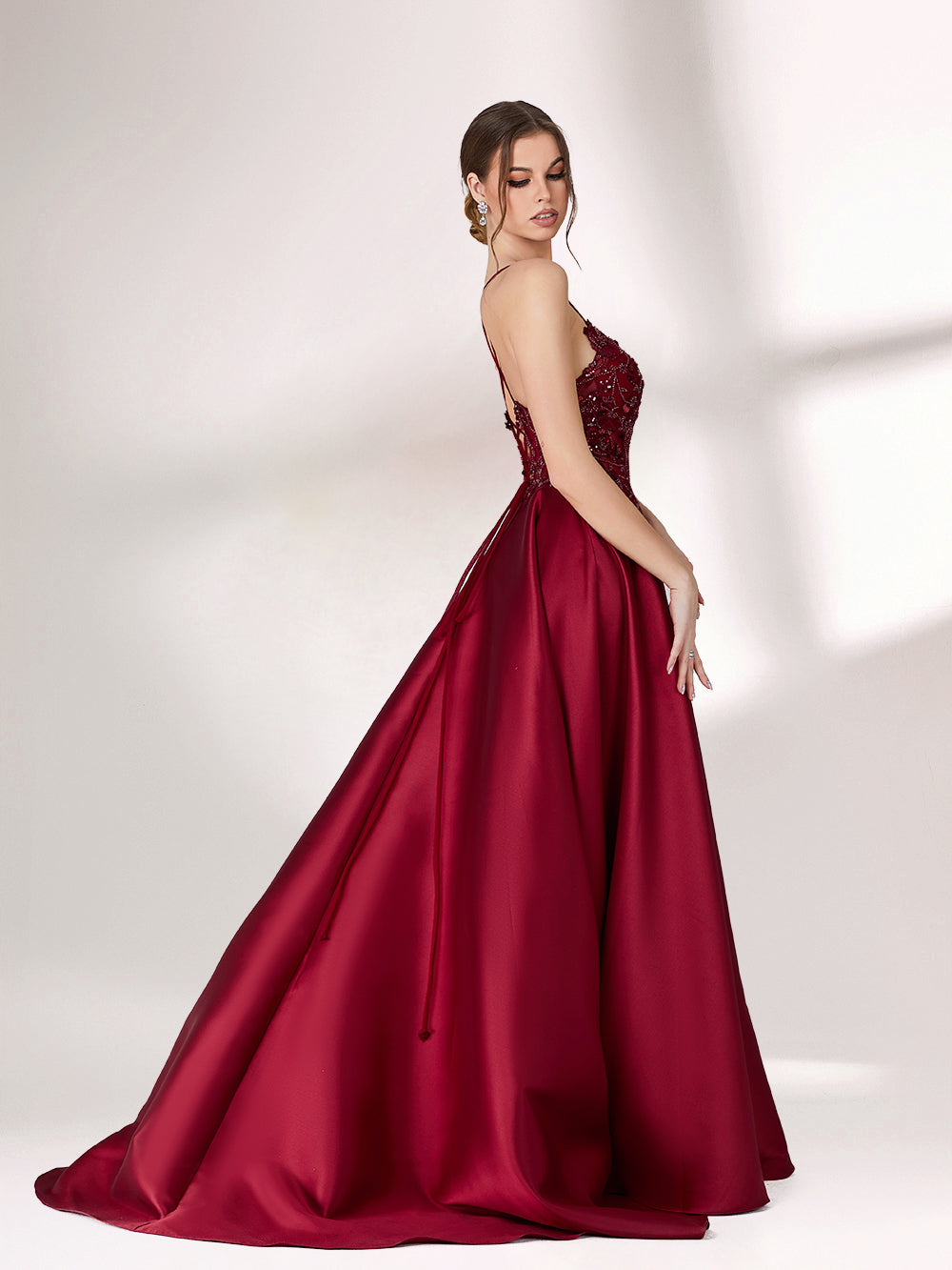 Bathed in soft light, a woman radiates elegance in a burgundy evening gown. With satin fabric, spaghetti straps, and lace embroidery, it crafts a luxurious and refined look for formal events.3