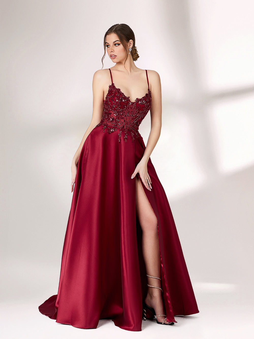 Bathed in soft light, a woman radiates elegance in a burgundy evening gown. With satin fabric, spaghetti straps, and lace embroidery, it crafts a luxurious and refined look for formal events.2