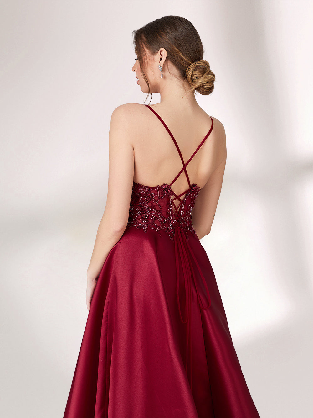 Bathed in soft light, a woman radiates elegance in a burgundy evening gown. With satin fabric, spaghetti straps, and lace embroidery, it crafts a luxurious and refined look for formal events.6