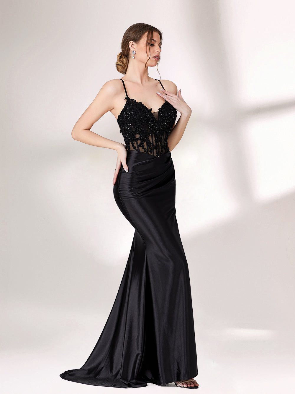 A woman stands against a light background, wearing a black evening gown. It features thin spaghetti straps, a deep V - neckline, intricate black bead and sequin embroidery on a sheer mesh upper, and a sleek satin skirt with a high side slit. The elegant design creates a glamorous and alluring look, perfect for formal events like galas or evening parties.3
