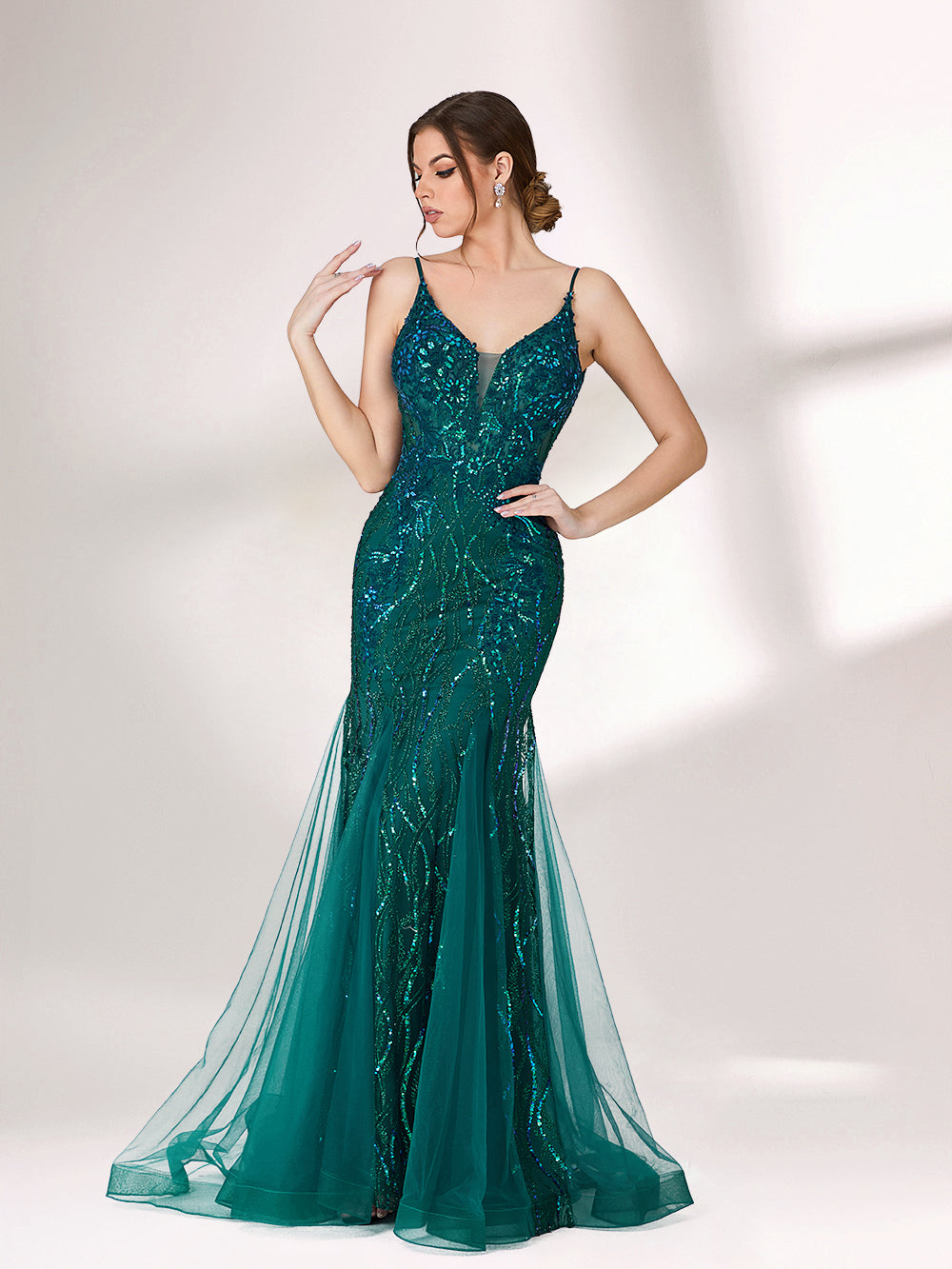 In soft lighting, a woman shines in a dark green evening gown. With sequin details, a mermaid silhouette, and tulle skirt, it creates a glamorous and elegant look for formal events.1