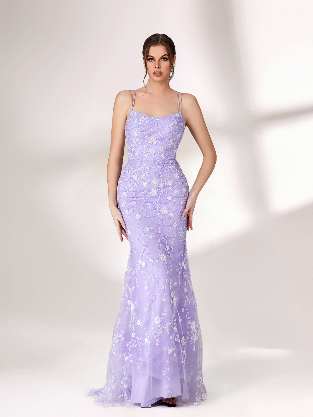 A woman stands against a light background, wearing a lavender mermaid - style evening gown. It has thin spaghetti straps, a sweetheart neckline, and is adorned with delicate white floral embroidery and beadwork throughout. The elegant design is perfect for formal events.6