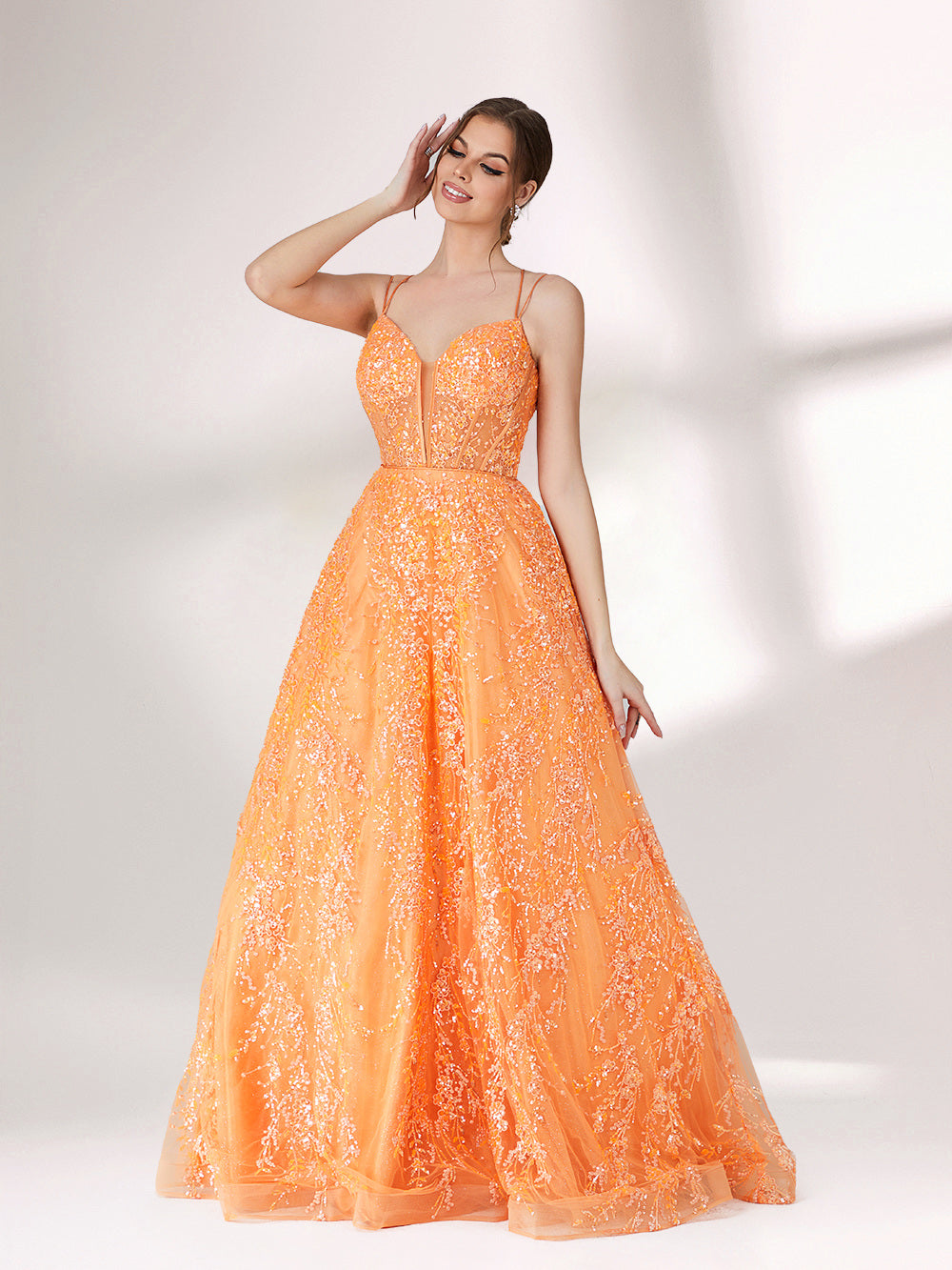 A woman stands against a light background, wearing an orange evening gown. It has thin spaghetti straps, a deep V - neckline, and is adorned with delicate floral - like sequin embroidery all over. The voluminous tulle skirt creates an elegant and glamorous look, perfect for formal events.1