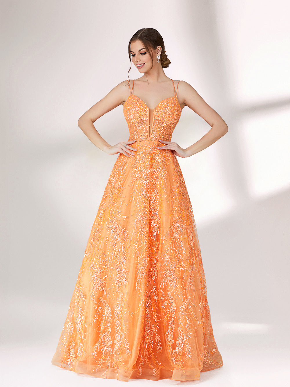 A woman stands against a light background, wearing an orange evening gown. It has thin spaghetti straps, a deep V - neckline, and is adorned with delicate floral - like sequin embroidery all over. The voluminous tulle skirt creates an elegant and glamorous look, perfect for formal events.4
