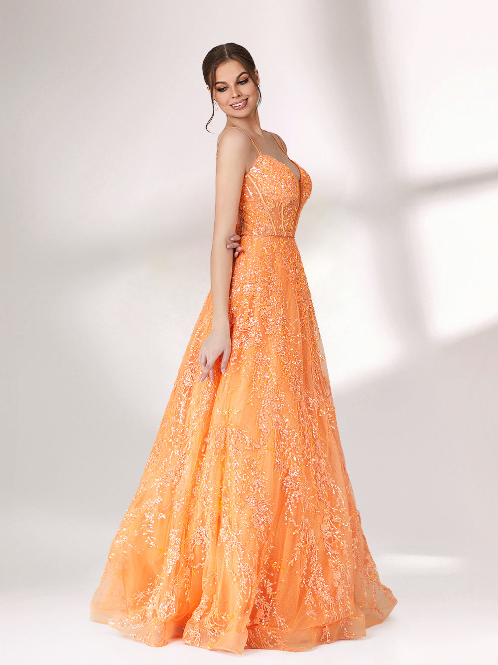 A woman stands against a light background, wearing an orange evening gown. It has thin spaghetti straps, a deep V - neckline, and is adorned with delicate floral - like sequin embroidery all over. The voluminous tulle skirt creates an elegant and glamorous look, perfect for formal events.3