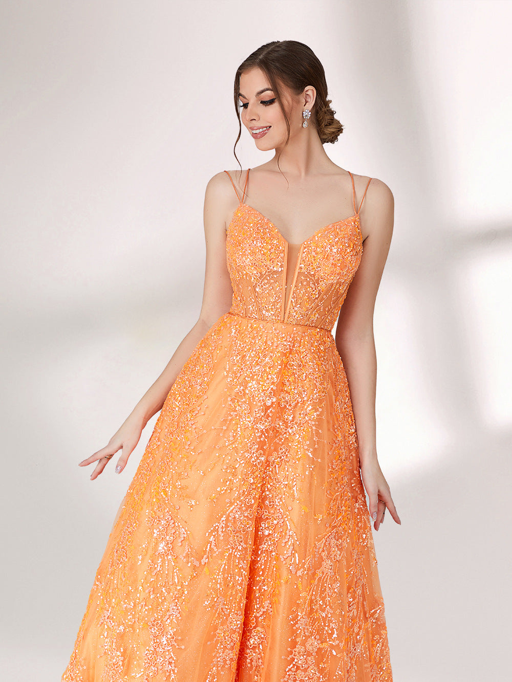 A woman stands against a light background, wearing an orange evening gown. It has thin spaghetti straps, a deep V - neckline, and is adorned with delicate floral - like sequin embroidery all over. The voluminous tulle skirt creates an elegant and glamorous look, perfect for formal events.5