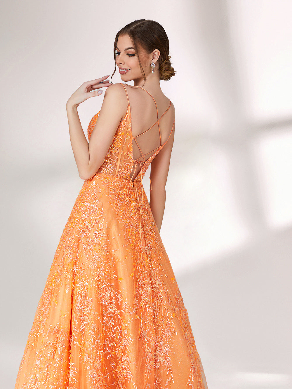 A woman stands against a light background, wearing an orange evening gown. It has thin spaghetti straps, a deep V - neckline, and is adorned with delicate floral - like sequin embroidery all over. The voluminous tulle skirt creates an elegant and glamorous look, perfect for formal events.56