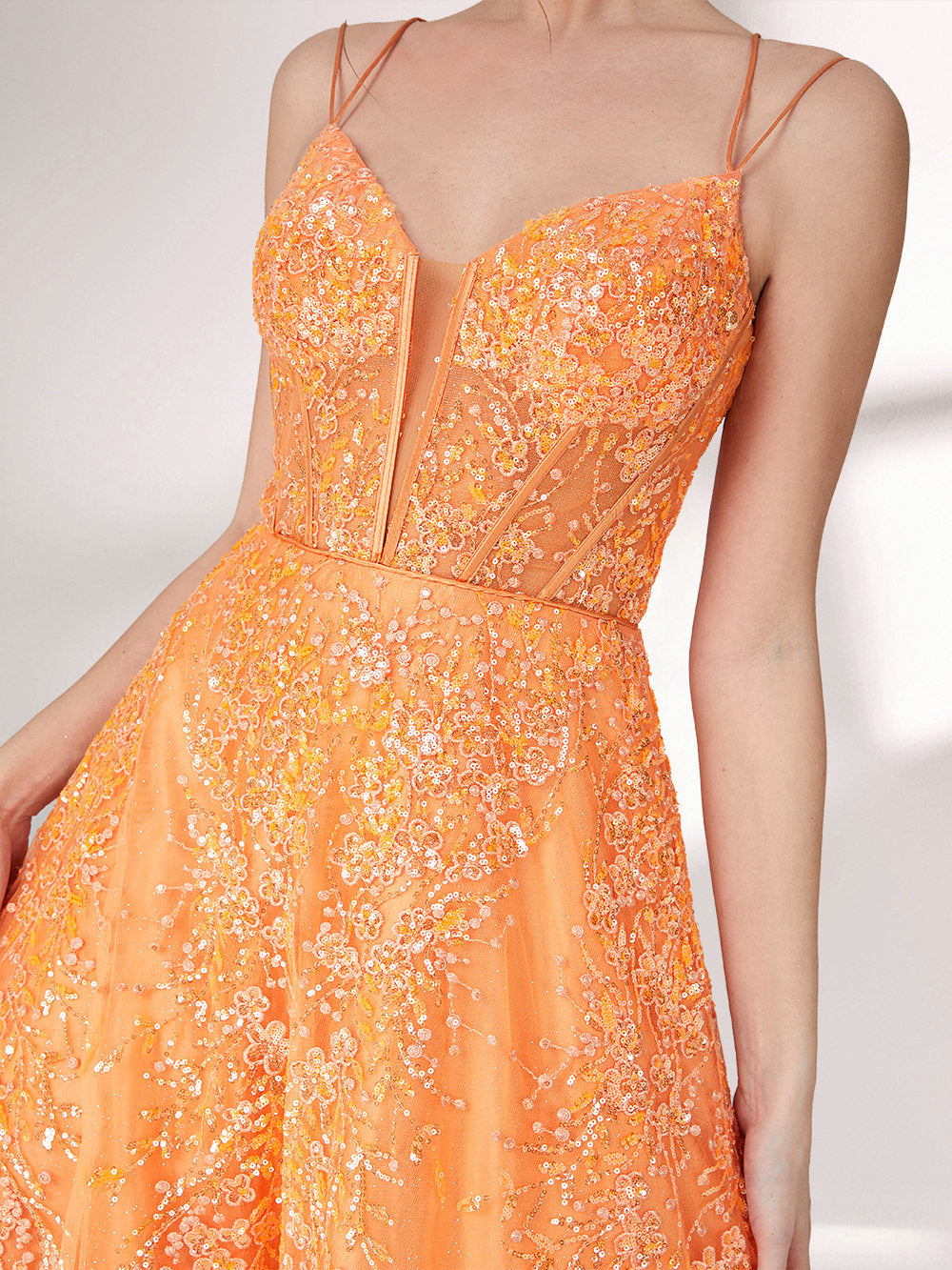 A woman stands against a light background, wearing an orange evening gown. It has thin spaghetti straps, a deep V - neckline, and is adorned with delicate floral - like sequin embroidery all over. The voluminous tulle skirt creates an elegant and glamorous look, perfect for formal events.7