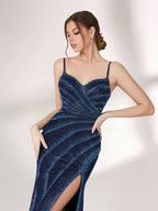 A woman stands against a light background, wearing a navy blue evening gown. It features thin spaghetti straps, a deep V - neckline, and diagonal stripes of shimmering blue embellishments. The dress has a high side slit, creating an elegant and sexy look, perfect for formal events.6