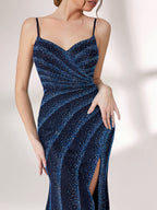A woman stands against a light background, wearing a navy blue evening gown. It features thin spaghetti straps, a deep V - neckline, and diagonal stripes of shimmering blue embellishments. The dress has a high side slit, creating an elegant and sexy look, perfect for formal events.7