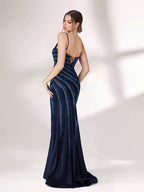 A woman stands against a light background, wearing a navy blue evening gown. It features thin spaghetti straps, a deep V - neckline, and diagonal stripes of shimmering blue embellishments. The dress has a high side slit, creating an elegant and sexy look, perfect for formal events.2