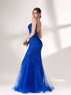 A woman stands against a light background, wearing a bright blue mermaid - style evening gown. It features thin spaghetti straps, a sheer panel at the neckline, and is covered in sparkling sequins. The tulle skirt flares out elegantly, creating a glamorous look perfect for formal events.2