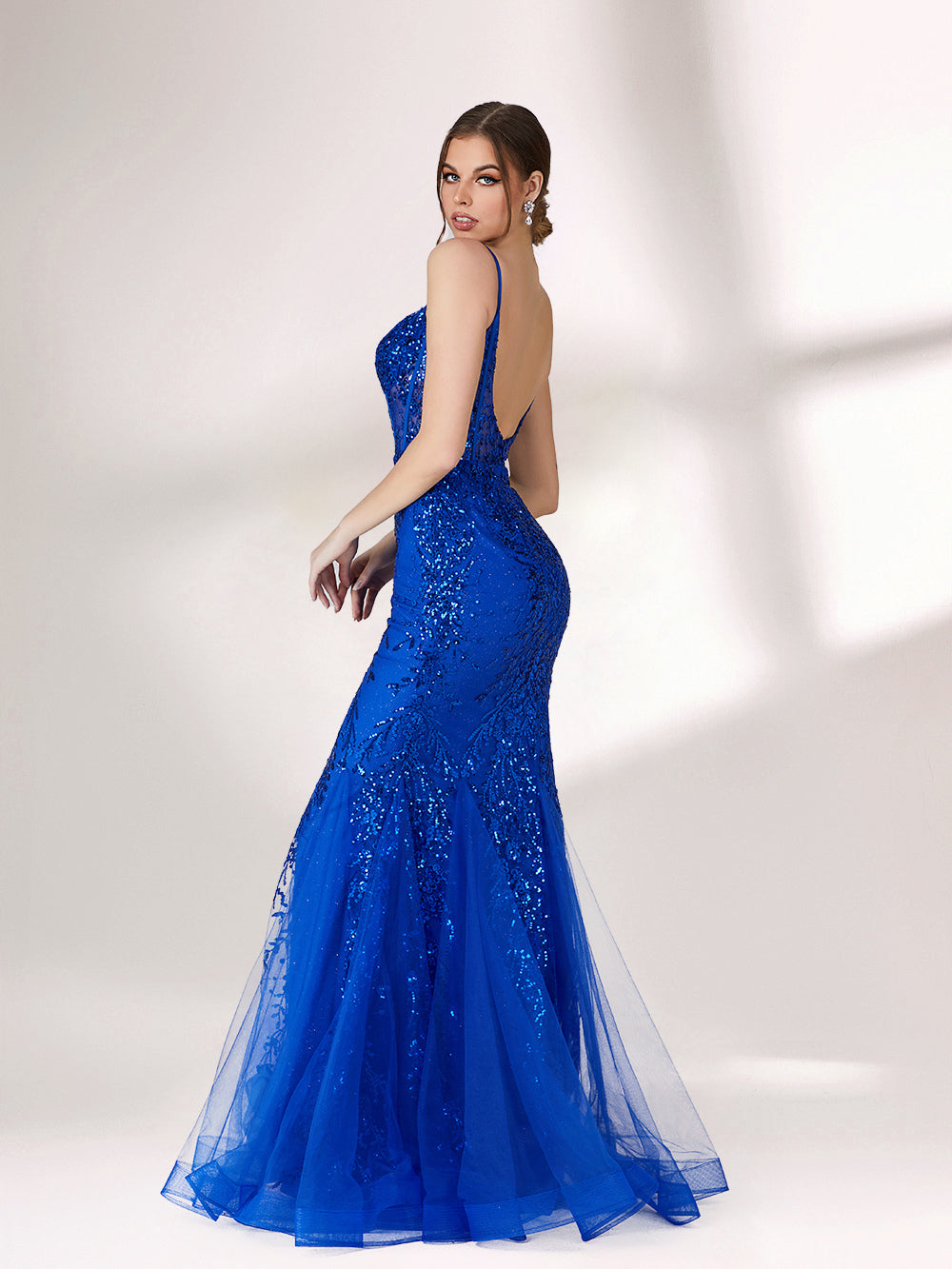 A woman stands against a light background, wearing a bright blue mermaid - style evening gown. It features thin spaghetti straps, a sheer panel at the neckline, and is covered in sparkling sequins. The tulle skirt flares out elegantly, creating a glamorous look perfect for formal events.2