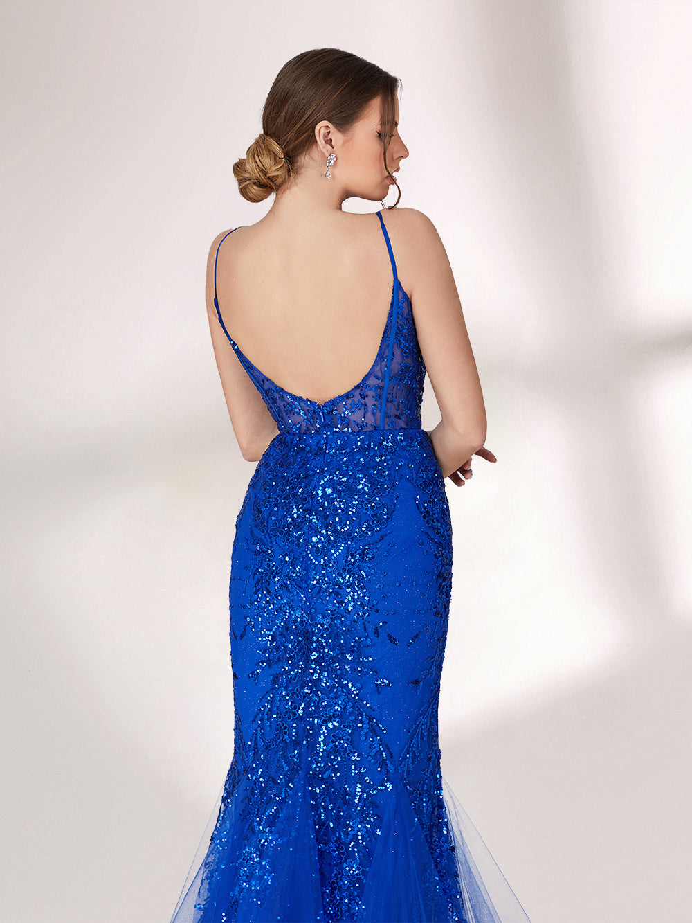 A woman stands against a light background, wearing a bright blue mermaid - style evening gown. It features thin spaghetti straps, a sheer panel at the neckline, and is covered in sparkling sequins. The tulle skirt flares out elegantly, creating a glamorous look perfect for formal events.4