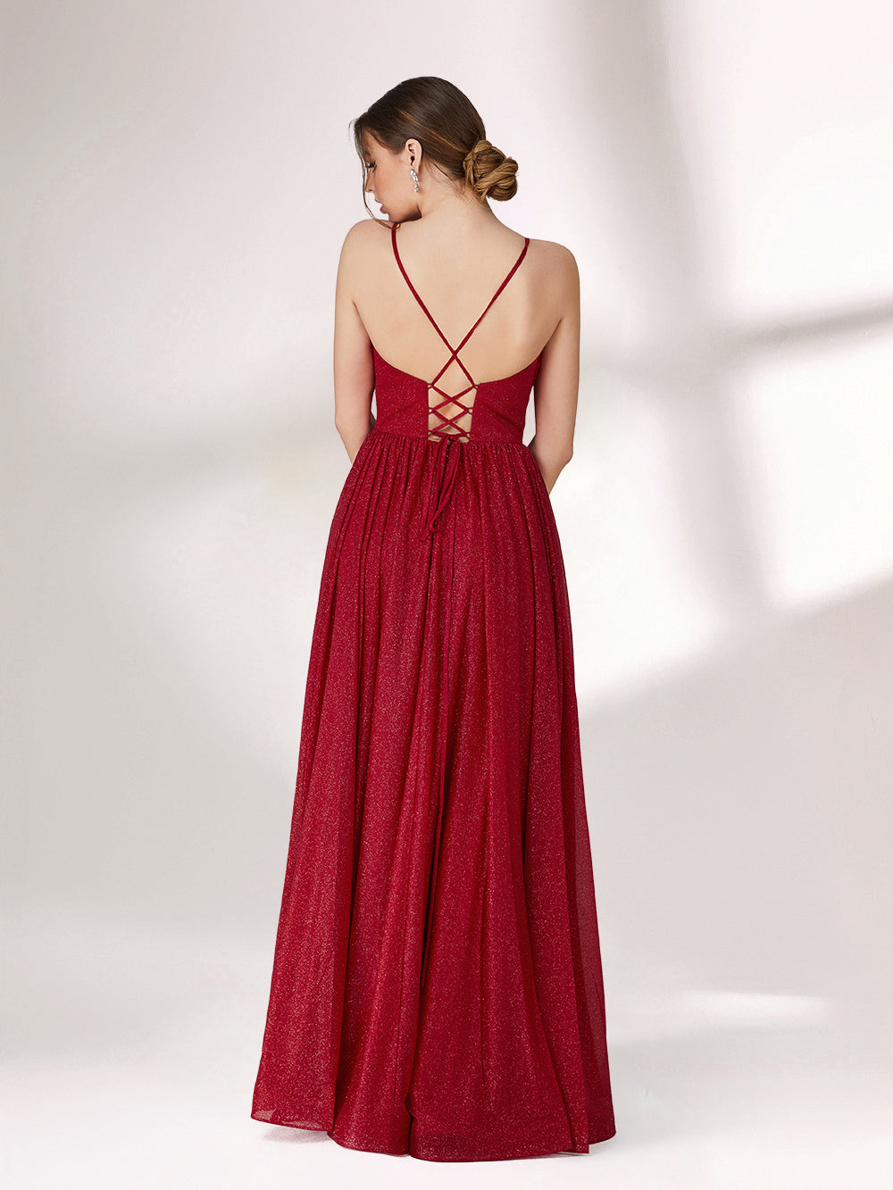 A woman stands against a light background, wearing a deep red evening gown. It has thin spaghetti straps, a deep V - neckline, and a voluminous skirt with a shimmering texture, creating an elegant and glamorous look, perfect for formal events.4