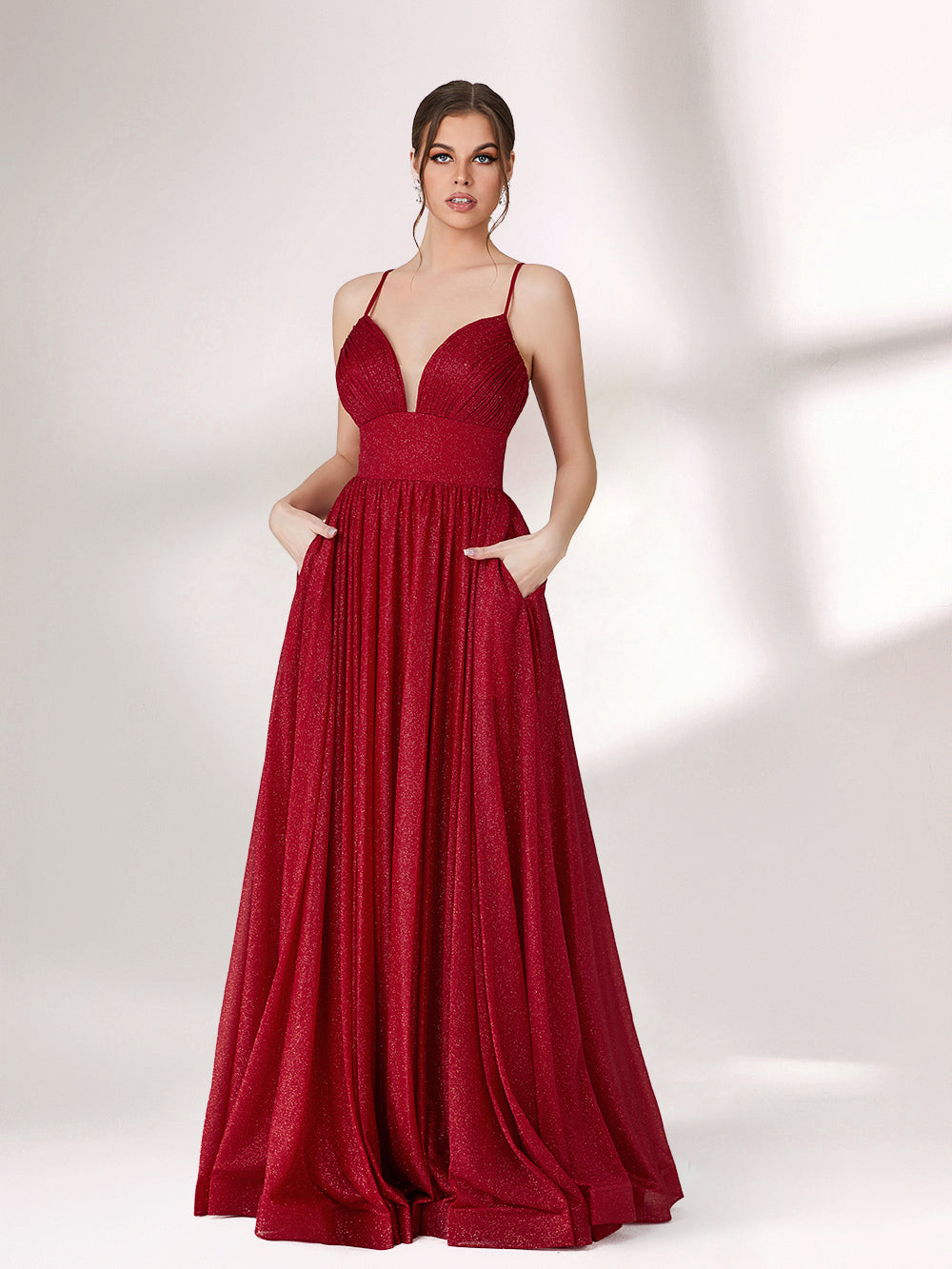 A woman stands against a light background, wearing a deep red evening gown. It has thin spaghetti straps, a deep V - neckline, and a voluminous skirt with a shimmering texture, creating an elegant and glamorous look, perfect for formal events.5