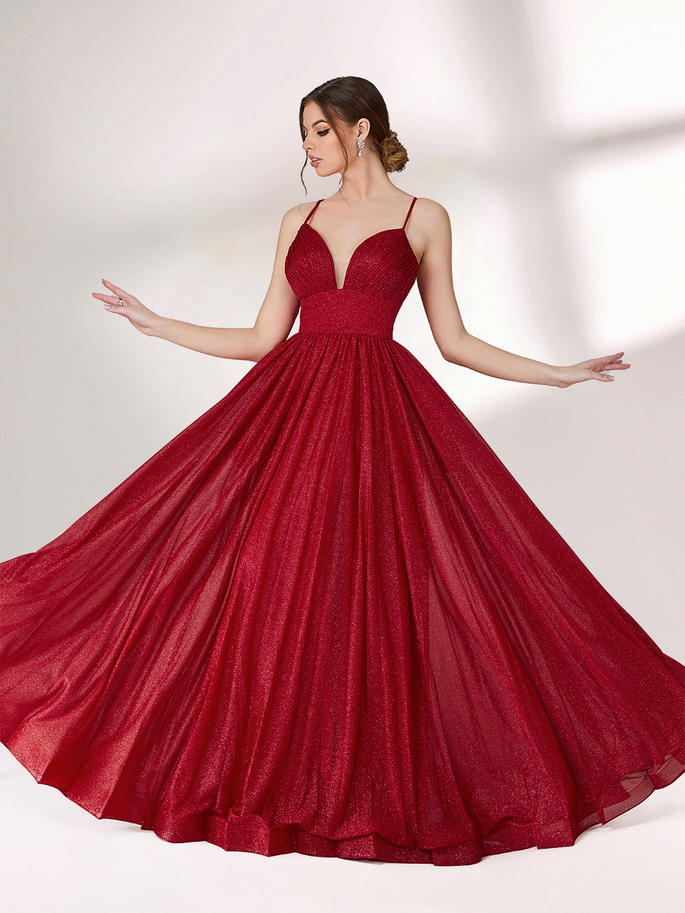 A woman stands against a light background, wearing a deep red evening gown. It has thin spaghetti straps, a deep V - neckline, and a voluminous skirt with a shimmering texture, creating an elegant and glamorous look, perfect for formal events.1